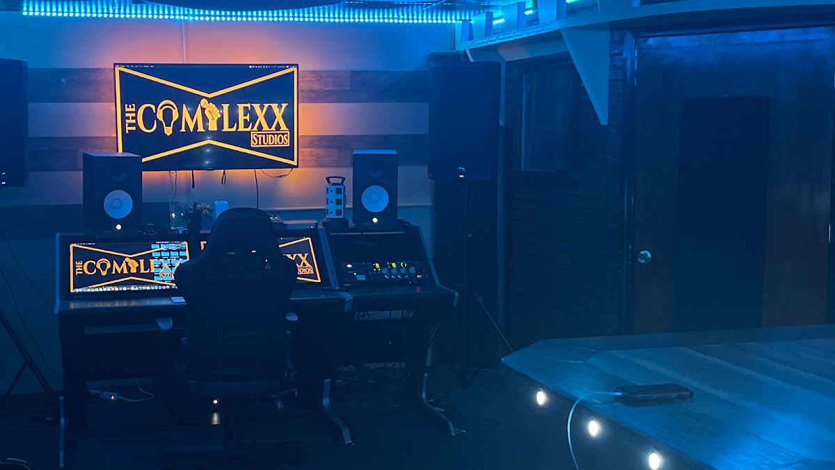 The recording studio at The Complexx ATL with a mixing console, monitors, and the studio's neon sign